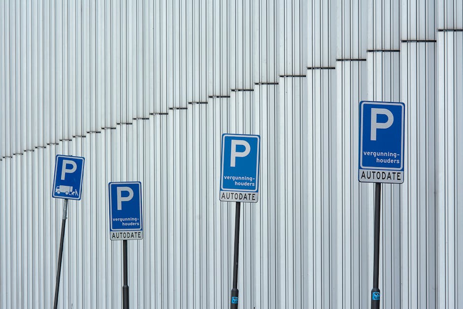 Four blue parking permit signs on black metal posts are positioned in front of a large metallic wall with vertical ridges. The signs display a white 'P' symbol and include additional text such as 'vergunninghouders' and 'AUTodate.' The signs are aligned along a pavement area outside a building, with some signs slightly tilted. The environment appears well-lit, highlighting the sleek, industrial exterior, and the signs may be related to parking regulations for moving or loading activities near Kew Gardens, as part of the house removals or furniture transport in the process of a home relocation. Man with Van North Sheen occasionally manages such parking permits as part of their moving logistics, ensuring compliance with loading bay rules during packing and loading procedures.