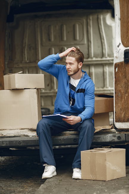 Two individuals are engaged in a home relocation process outside a residential property, with one person assisting by holding a cardboard box marked as fragile, while the other is loading the box onto
